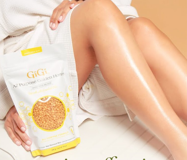 Gambe lisce e idratate accanto a una confezione di cera GiGi All Purpose Golden Honey, tenuta in mano da una donna in accappatoio.