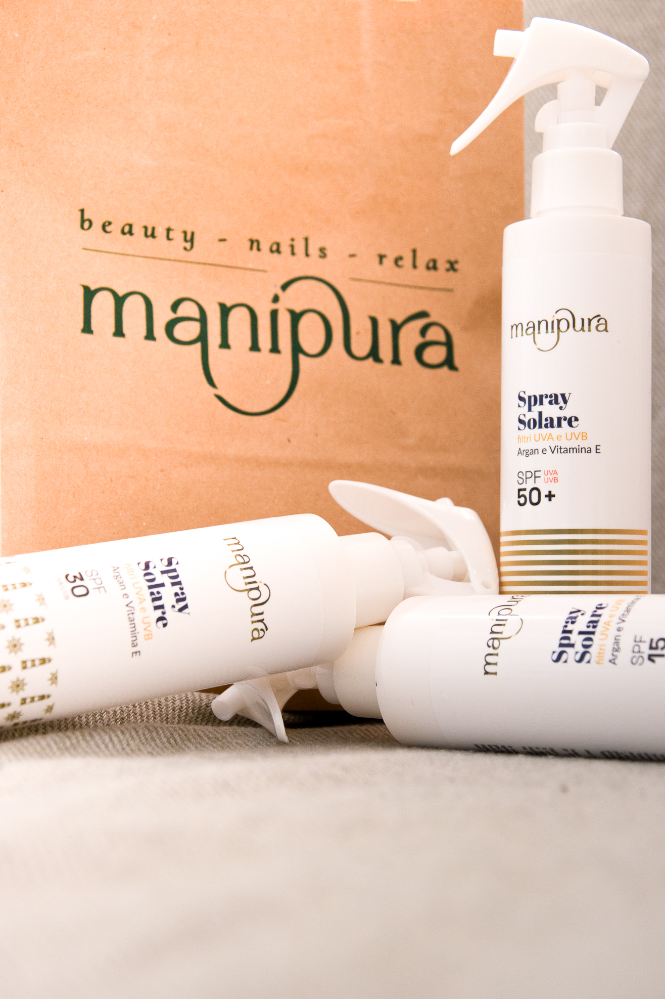 Spray solari Manipura con SPF 15, 30 e 50+ disposti davanti a una shopper del centro estetico.