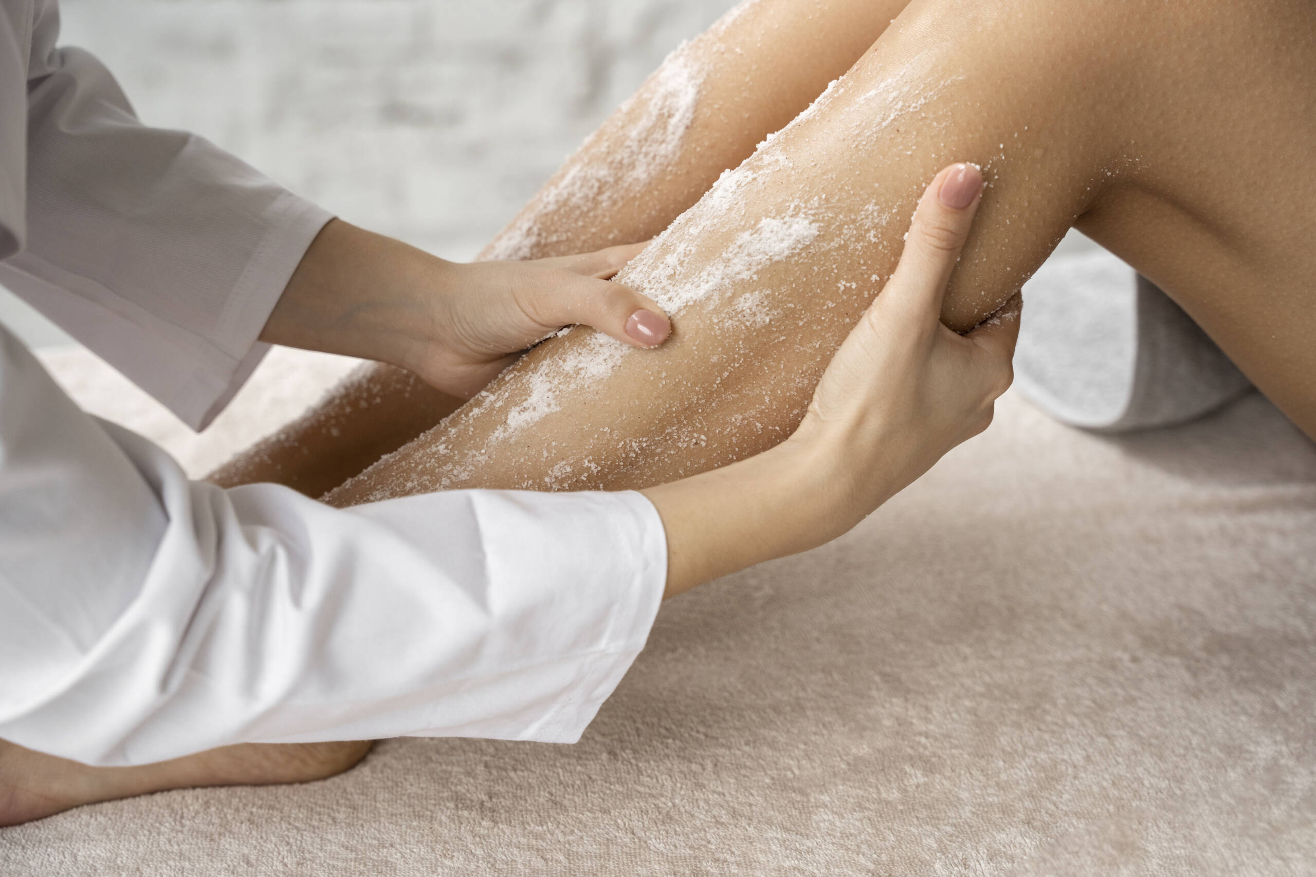 Applicazione di scrub esfoliante sulle gambe durante un trattamento corpo professionale.
