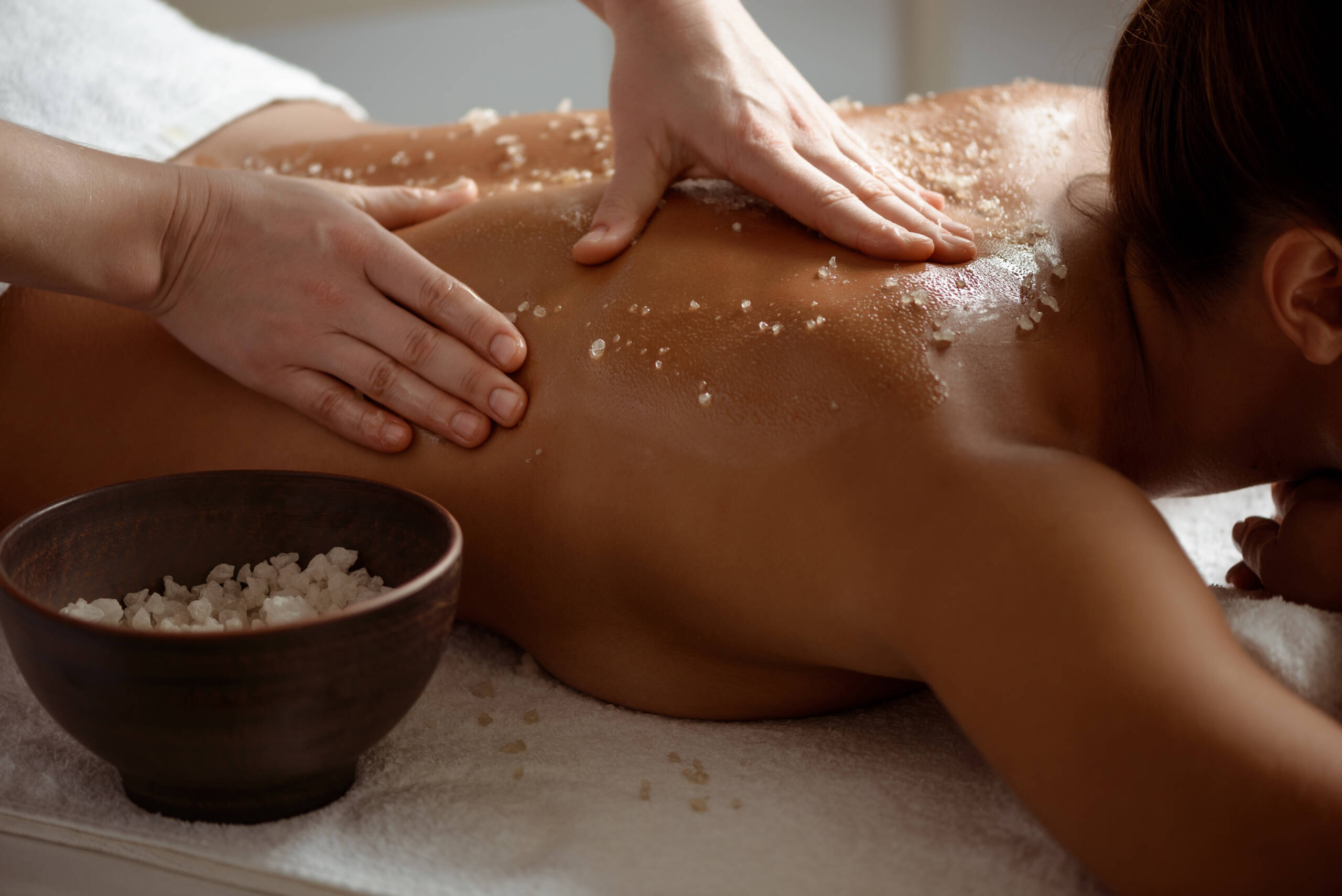 Massaggio esfoliante alla schiena con scrub salino durante un trattamento corpo professionale.