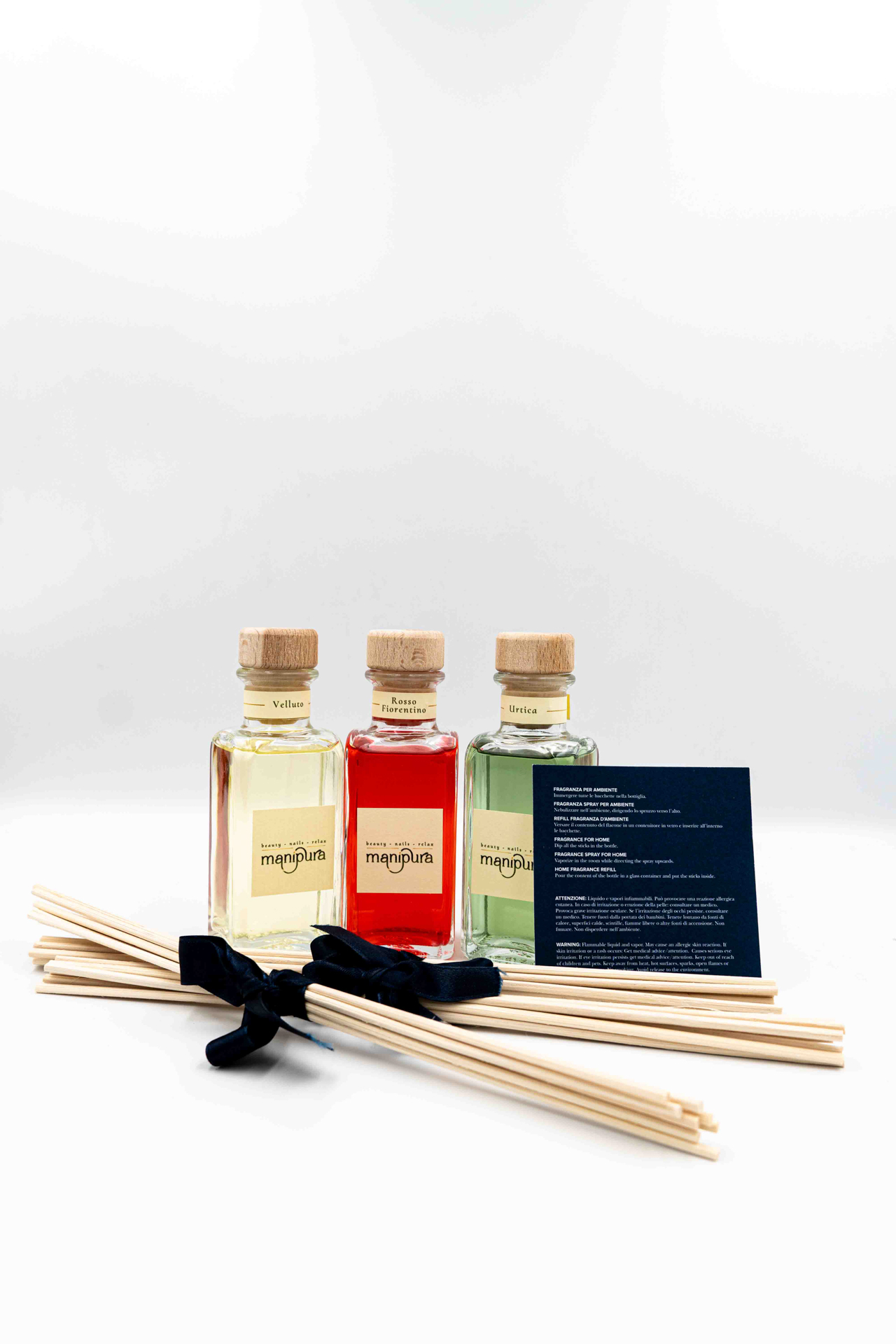 Set di profumatori ambiente Manipura in bottiglie di vetro con tappo in legno,accompagnati da bastoncini in legno e cartoncino informativo, su sfondo bianco.
