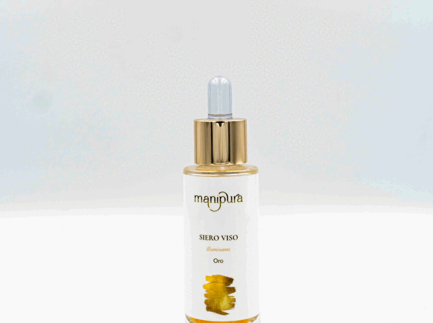 Boccetta aperta del siero viso illuminante Oro di Manipura con contagocce dorato appoggiato su sfondo bianco.
