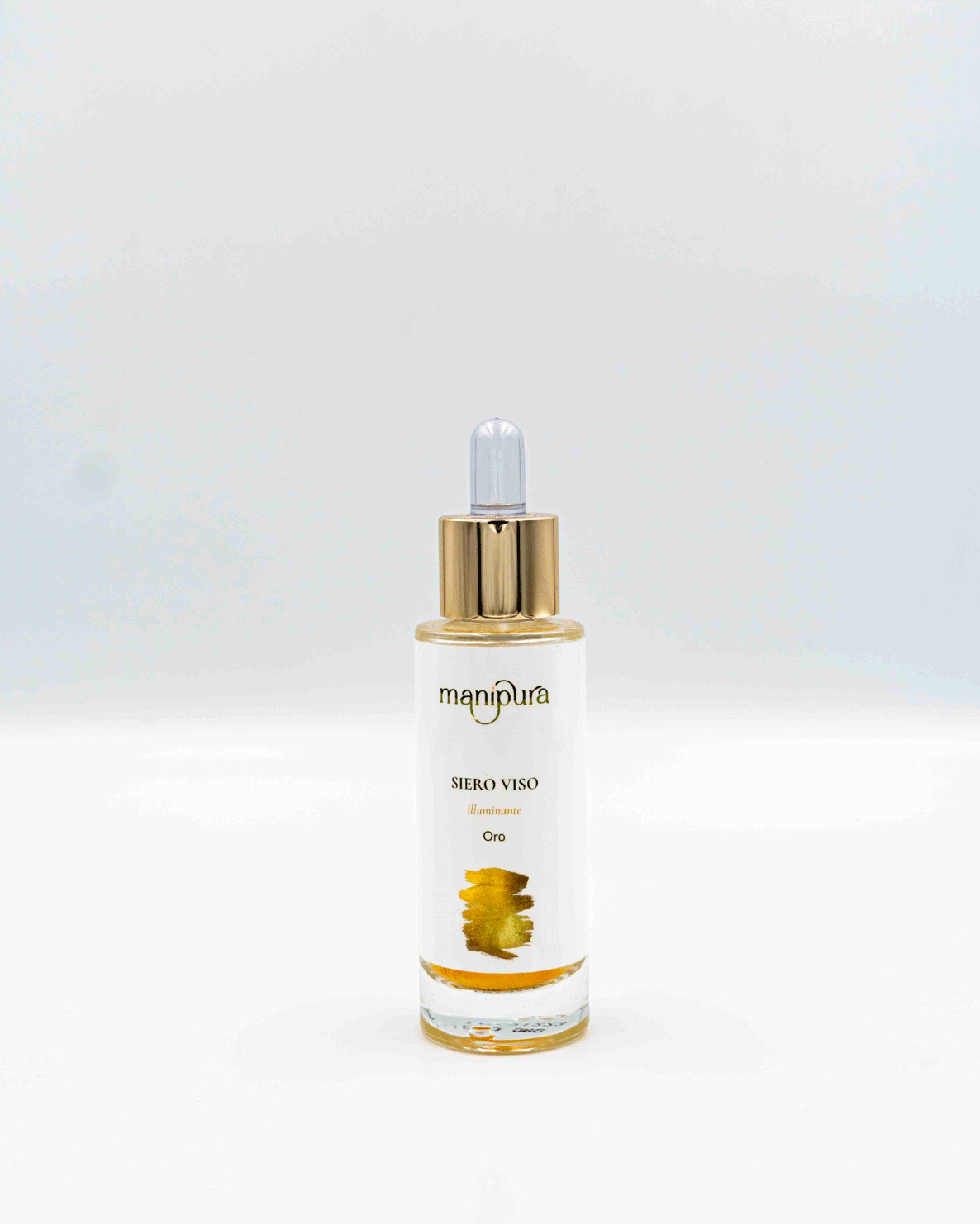 Boccetta aperta del siero viso illuminante Oro di Manipura con contagocce dorato appoggiato su sfondo bianco.
