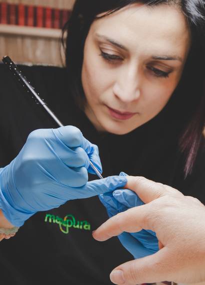 Onicotecnica che esegue una manicure professionale indossando guanti blu e lavorando con pennello di precisione.