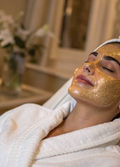 Donna rilassata con maschera viso dorata durante un trattamento skincare di lusso in un centro estetico.